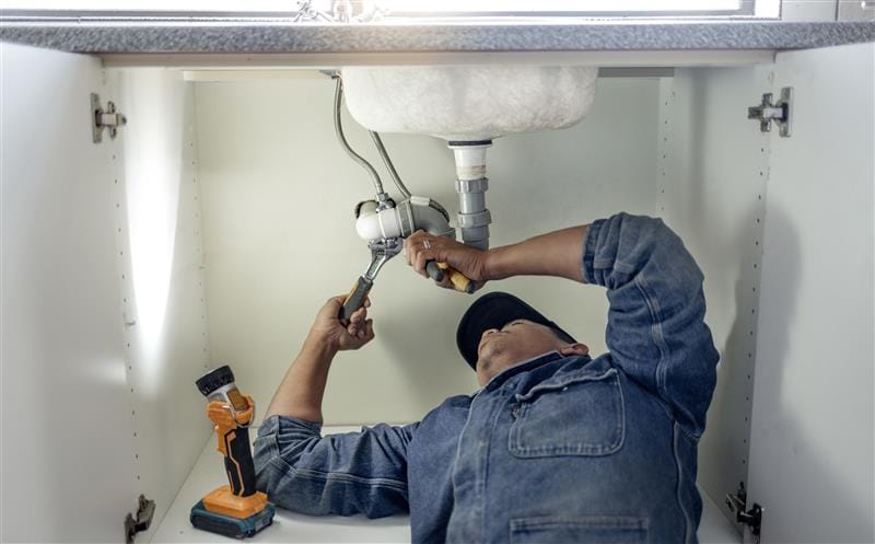 Plumber repairing pipes beneath a bathroom sink in San Bernardino