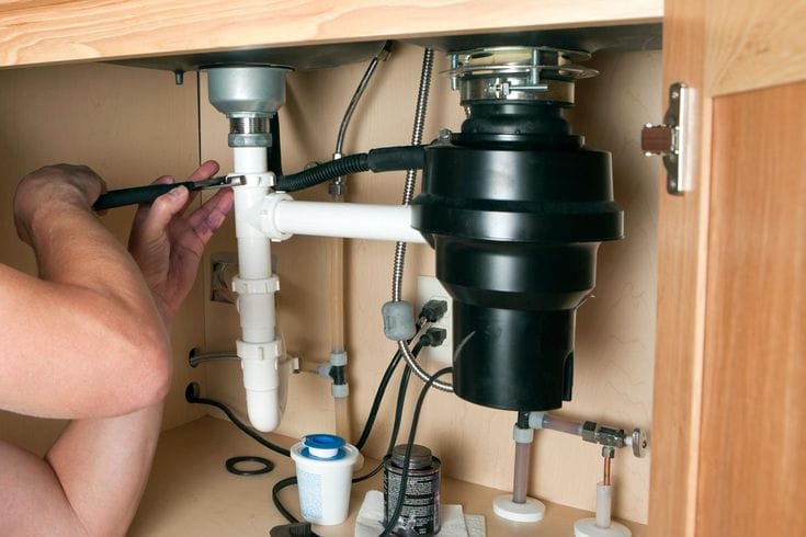 Plumber installing a garbage disposal beneath a kitchen sink in San Bernardino