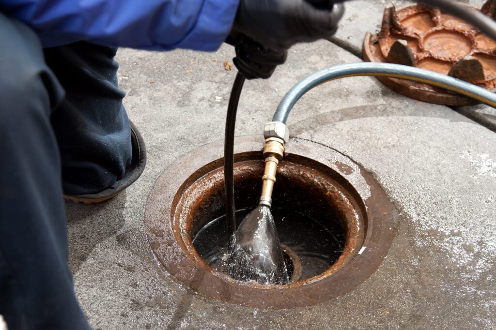 Plumber hydro jetting a sewer line through a manhole in San Bernardino