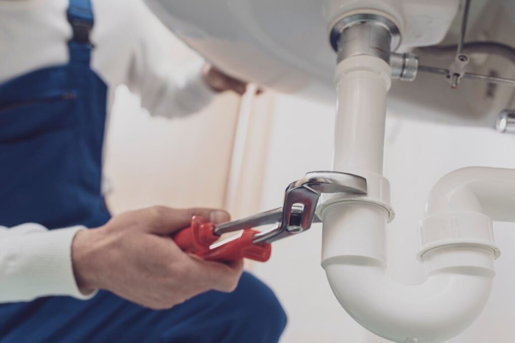 Plumber repairing a white drain pipe beneath a sink in San Bernardino