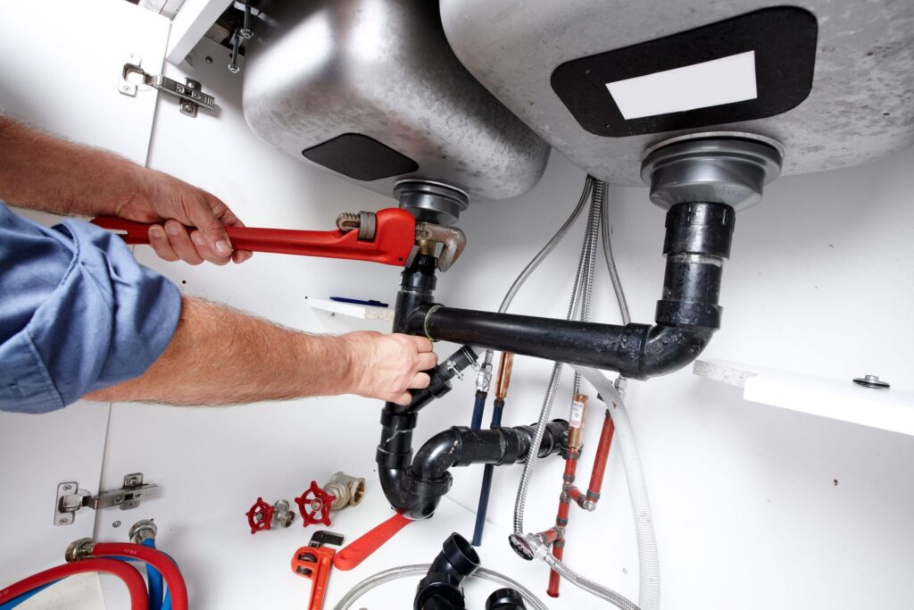 Plumber repairing drain pipes beneath a kitchen sink in San Bernardino